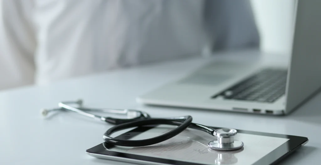 Medical stethoscope alongside a laptop and tablet, representing modern healthcare technology and digital records
