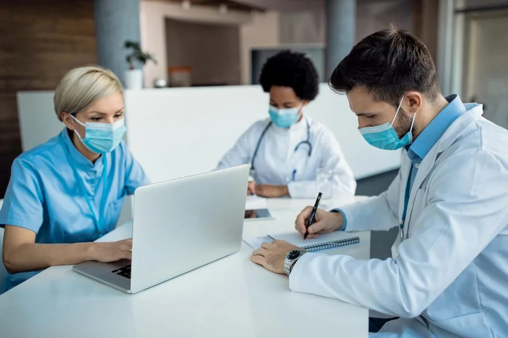Three masked healthcare workers reviewing notes together at a clinic desk
