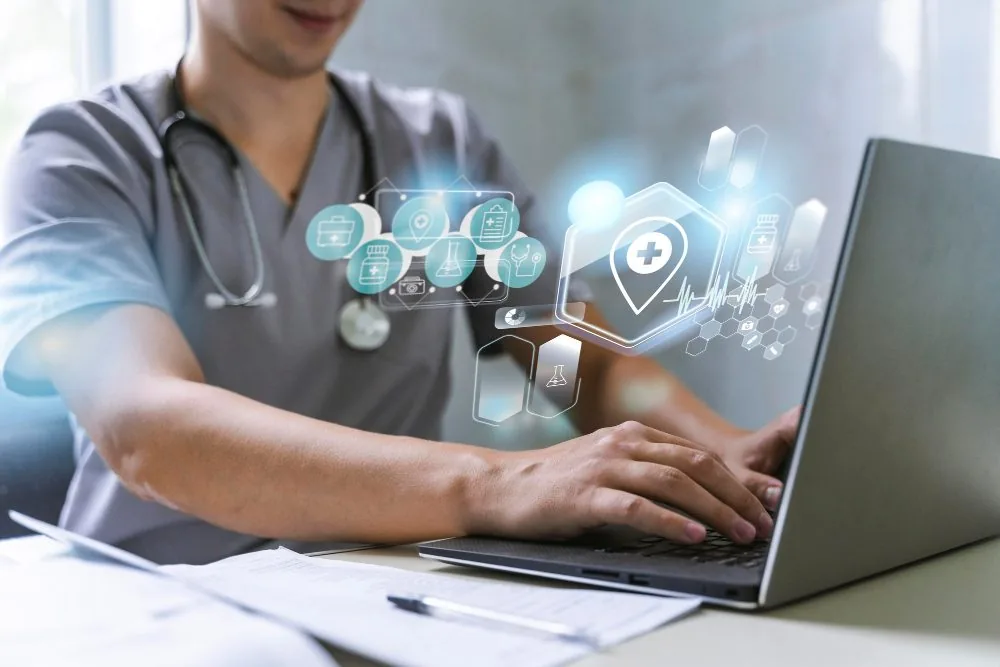 A clinician in scrubs typing on a laptop, overlaid with digital health icons