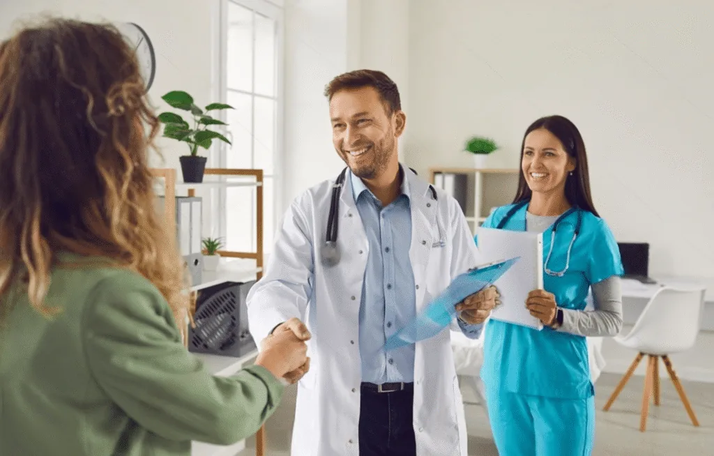A clinician shaking hands with a patient while a colleague looks on