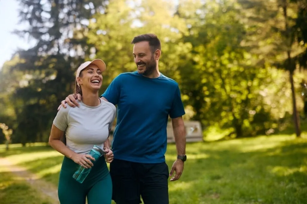 A couple in workout clothes walking together and laughing in a park