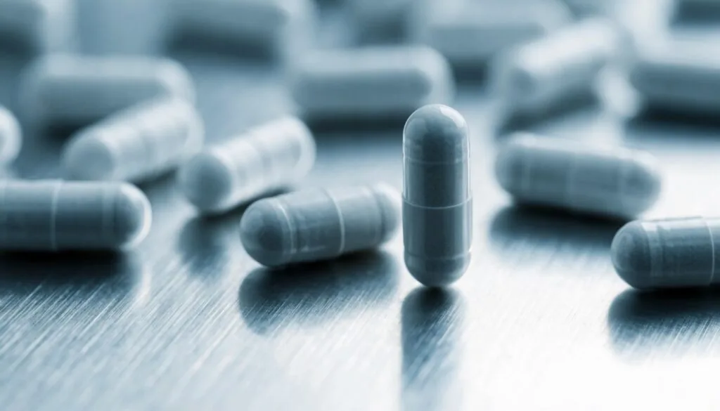 Plain white pharmaceutical capsules scattered on a brushed stainless steel surface